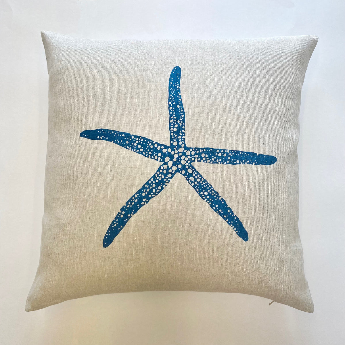 A handprinted square linen cushion with a large blue Starfish design
